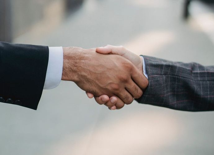 Two businessmen shaking hands outside, symbolizing cooperation and agreement in a city setting.